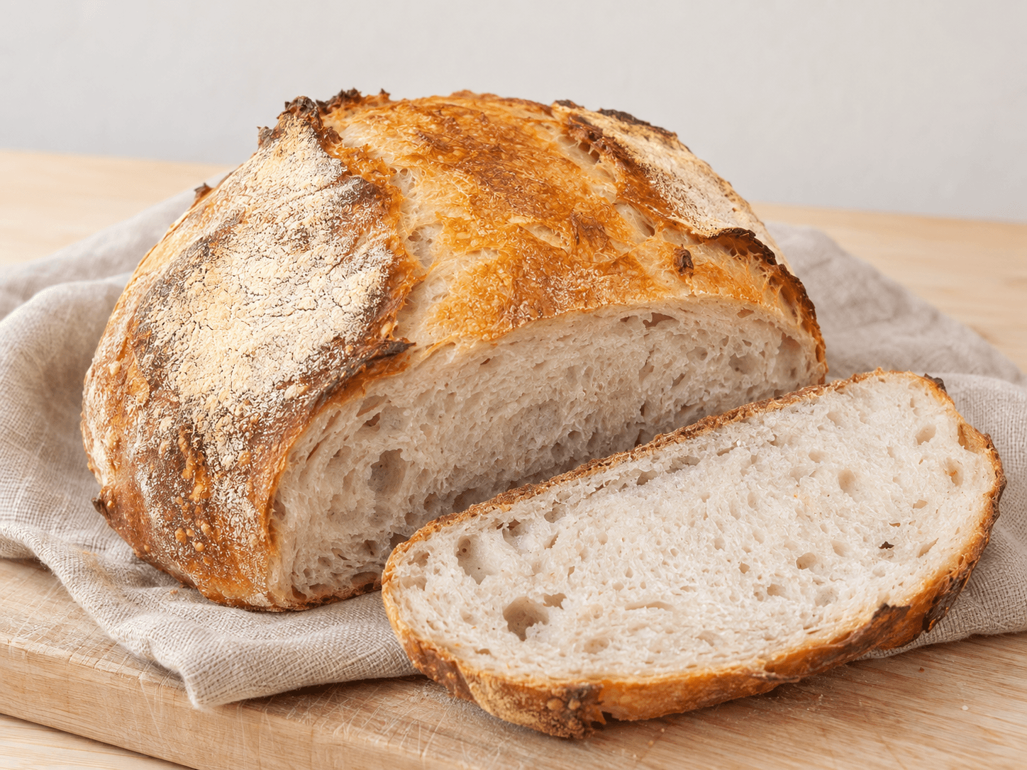 Bröd sourdough loaf with a cut slice on pale timber and oatmeal linen